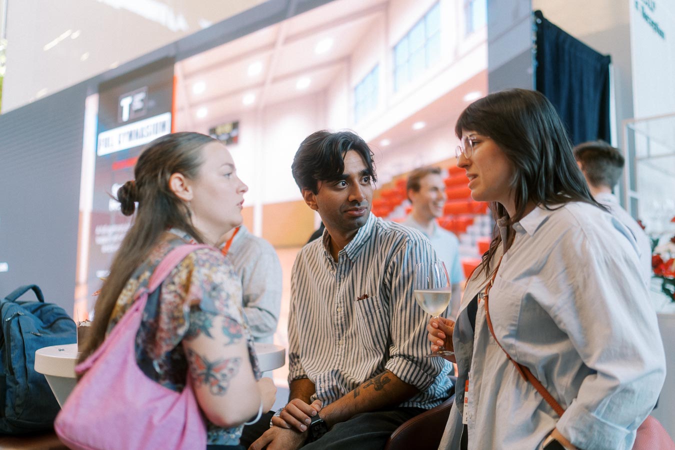 Three adults in conversation at the Toronto Prep Forever Launch Party at Ricarda’s, with event signage and red seating in the background.