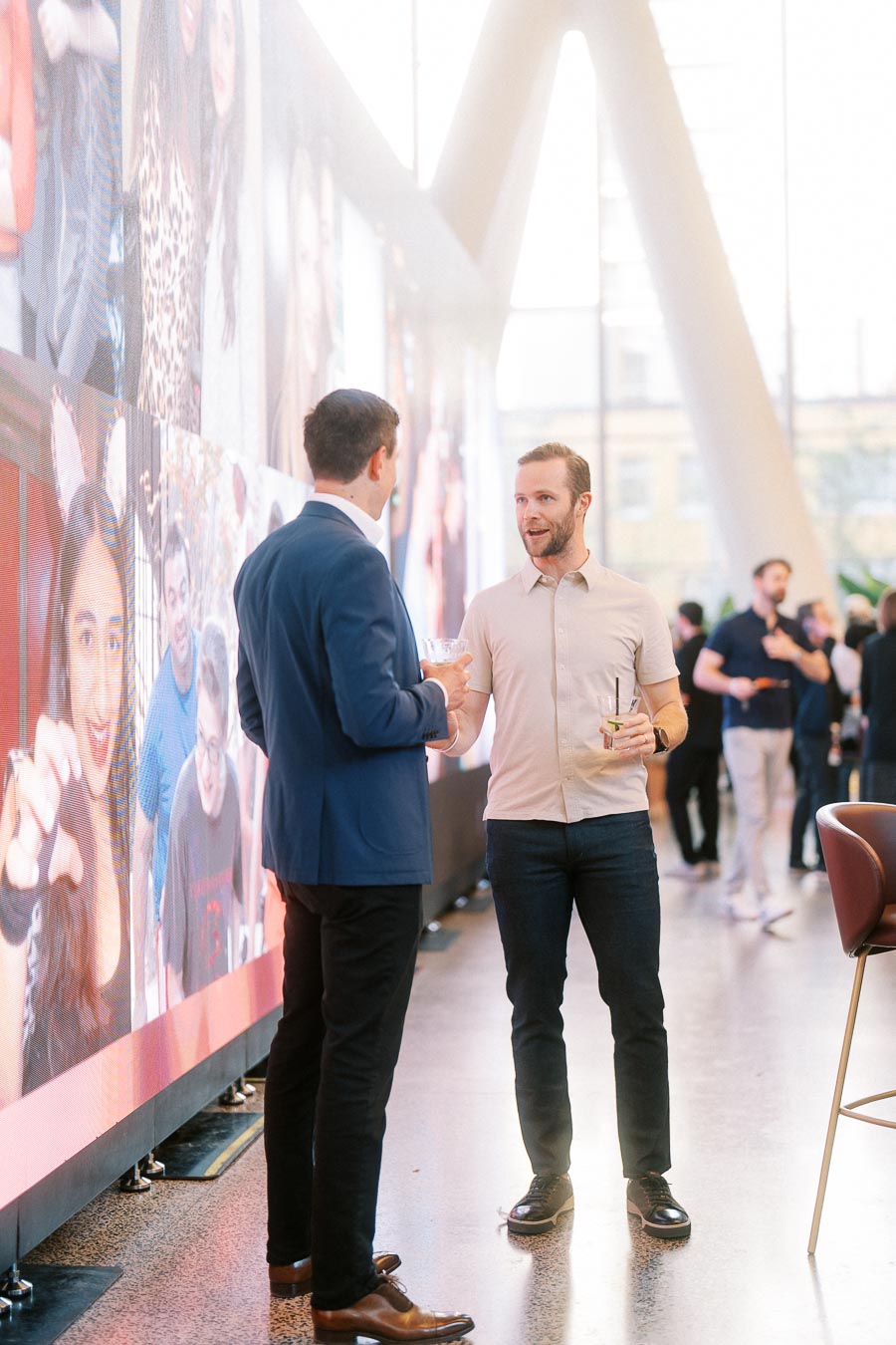 Two men in conversation holding drinks beside a digital photo wall at the Toronto Prep Forever Launch Party at Ricarda’s, Toronto.