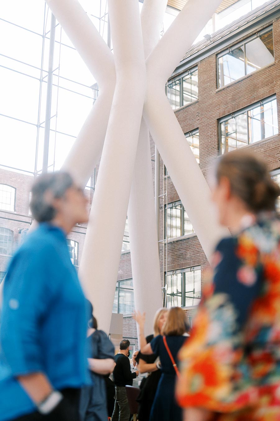 Blurry guests in foreground with focus on modern white structural columns and brick walls inside Ricarda’s Atrium in Toronto.