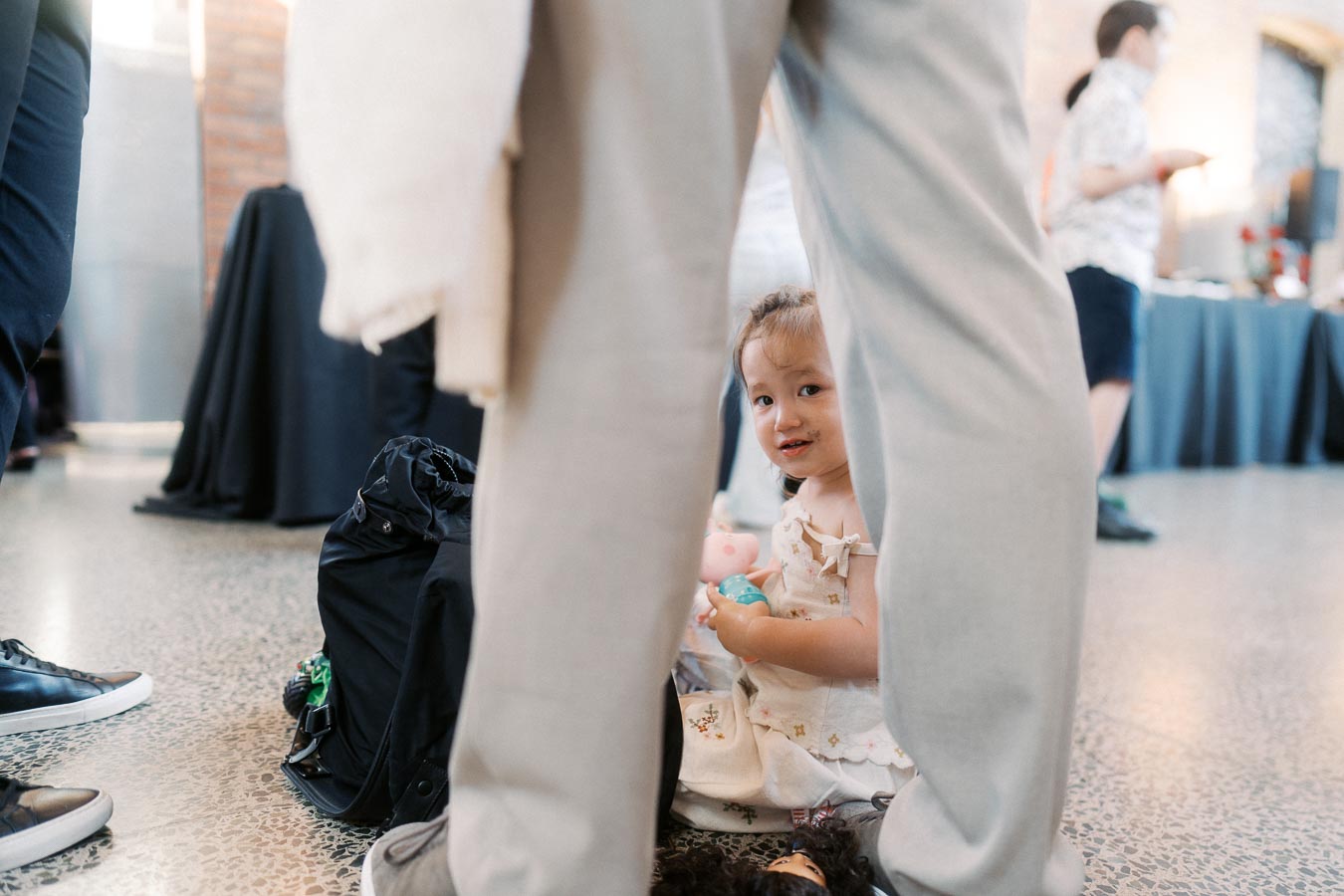 A young child sitting on the floor with toys, framed between adults' legs at a Toronto Prep School launch event at Ricarda’s.