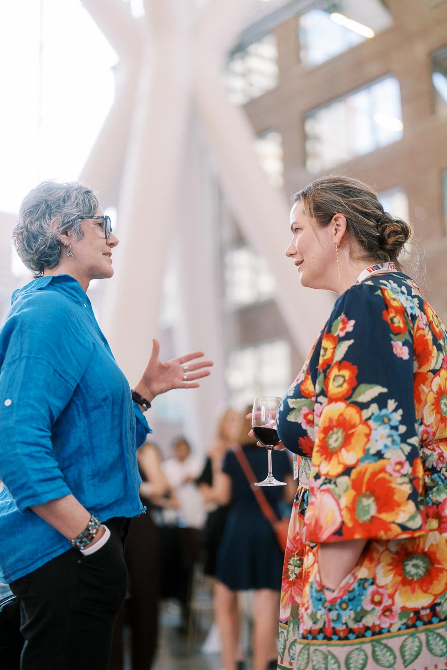 Two women converse at the Toronto Prep Forever Launch Party in The Atrium at Ricarda’s, Toronto, with modern architecture and event guests in the background.