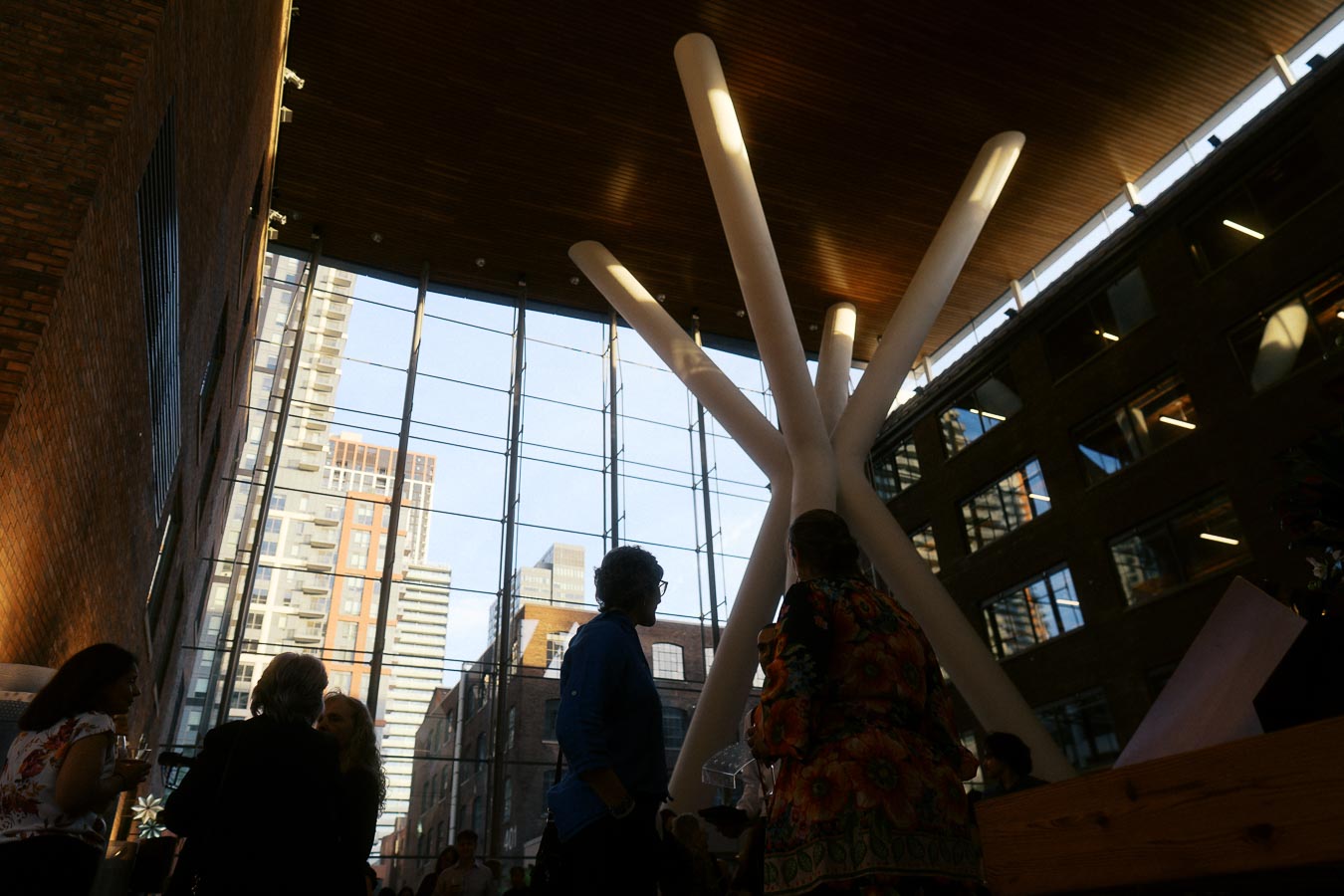 Guests socializing inside Ricarda’s Atrium in Toronto, featuring tall glass walls, unique white columns, and a cityscape backdrop at an event.