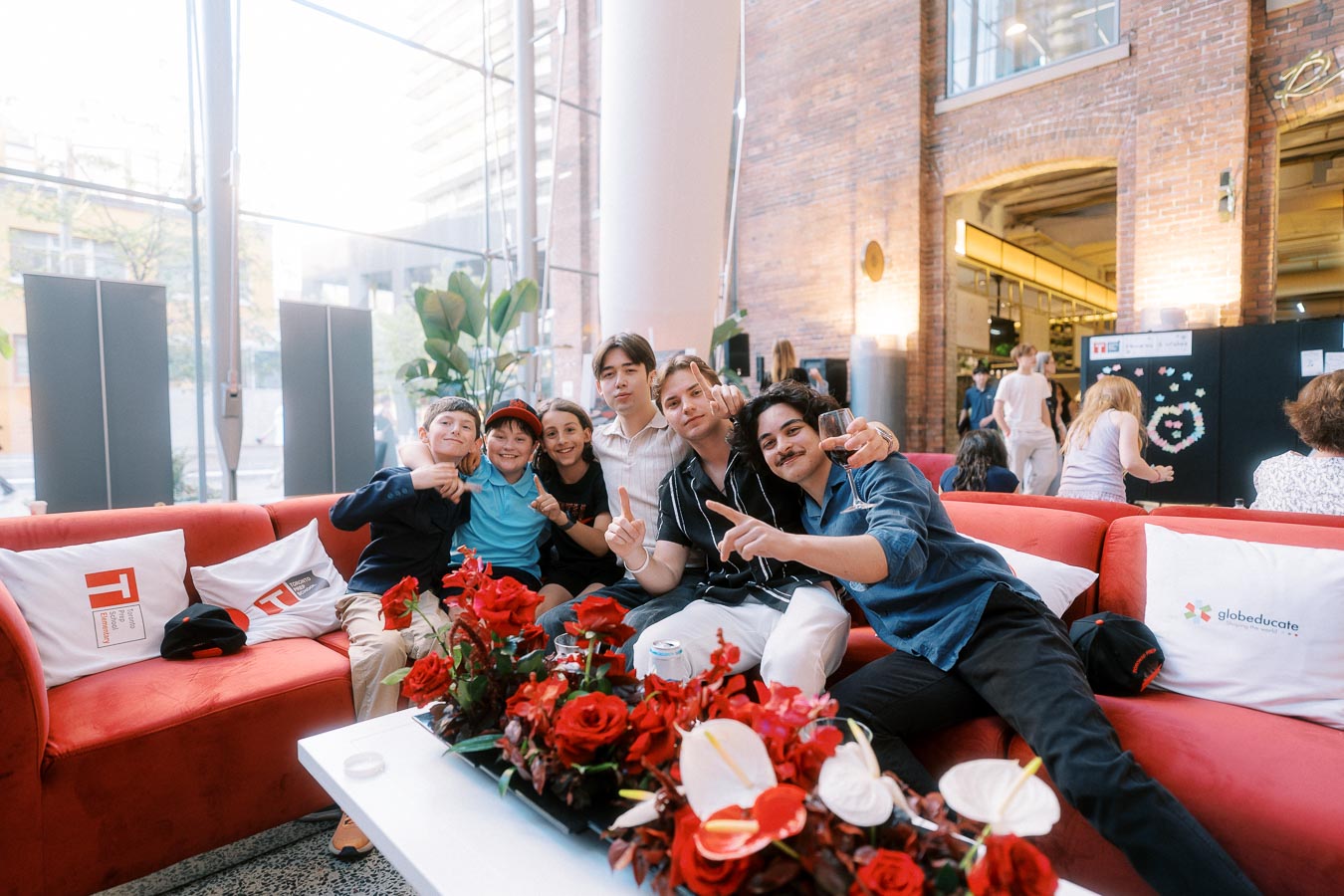 Group of Toronto Prep School students and alumni seated on a red couch, smiling and posing at Ricarda’s Atrium during the school’s launch event.