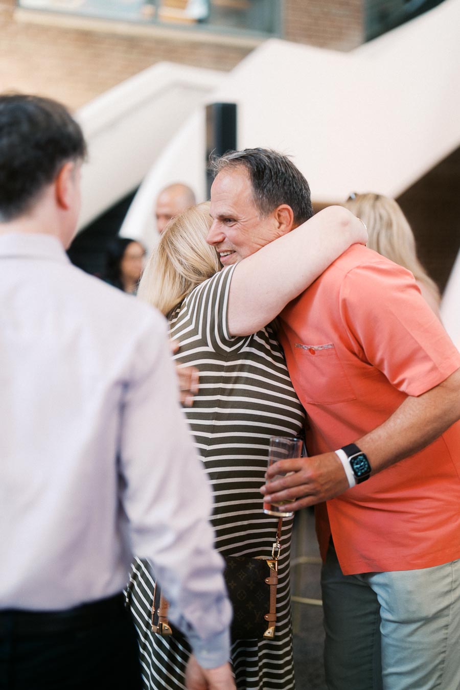 Two guests share a warm hug at the Toronto Prep Forever Launch Party at Ricarda’s, with others mingling in the modern atrium event space.