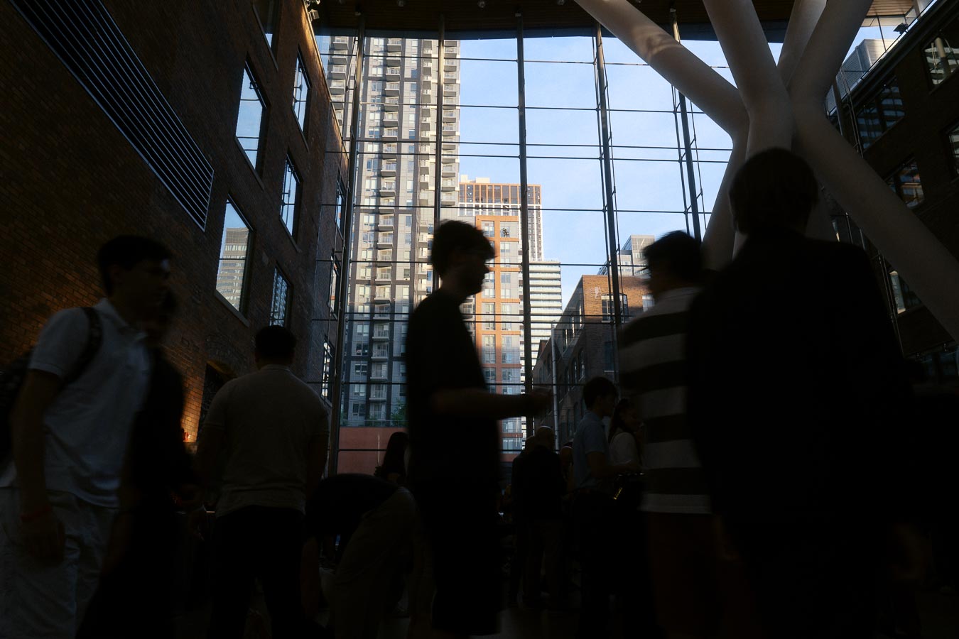 Silhouetted guests mingle inside Ricarda’s glass atrium in Toronto, with modern high-rise buildings visible through the large windows at dusk.