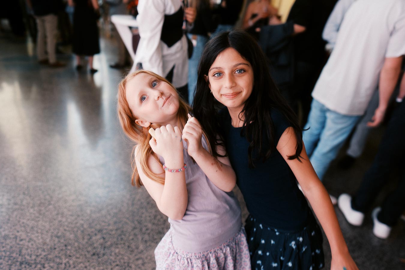 Two young girls smiling and holding hands at the Toronto Prep Forever Launch Party at Ricarda’s, surrounded by event guests.