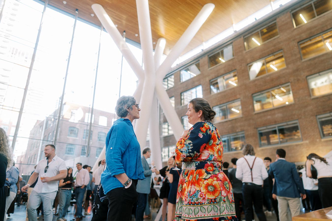 Two people conversing in a bright, modern atrium at Ricarda’s in Toronto during a school launch event, with guests mingling in the background.