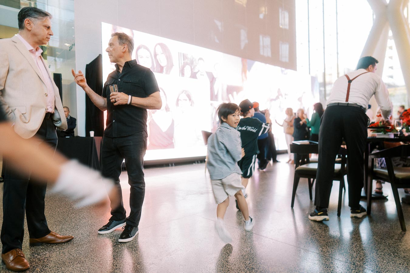 Guests converse while a child runs through the modern atrium at Ricarda’s during the Toronto Prep Forever Launch Party, highlighting a lively school community event.