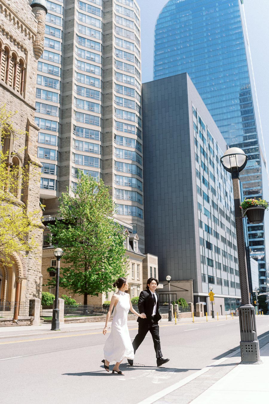 Couple holding hands and walking on a bright city street with old and modern buildings in downtown Toronto.