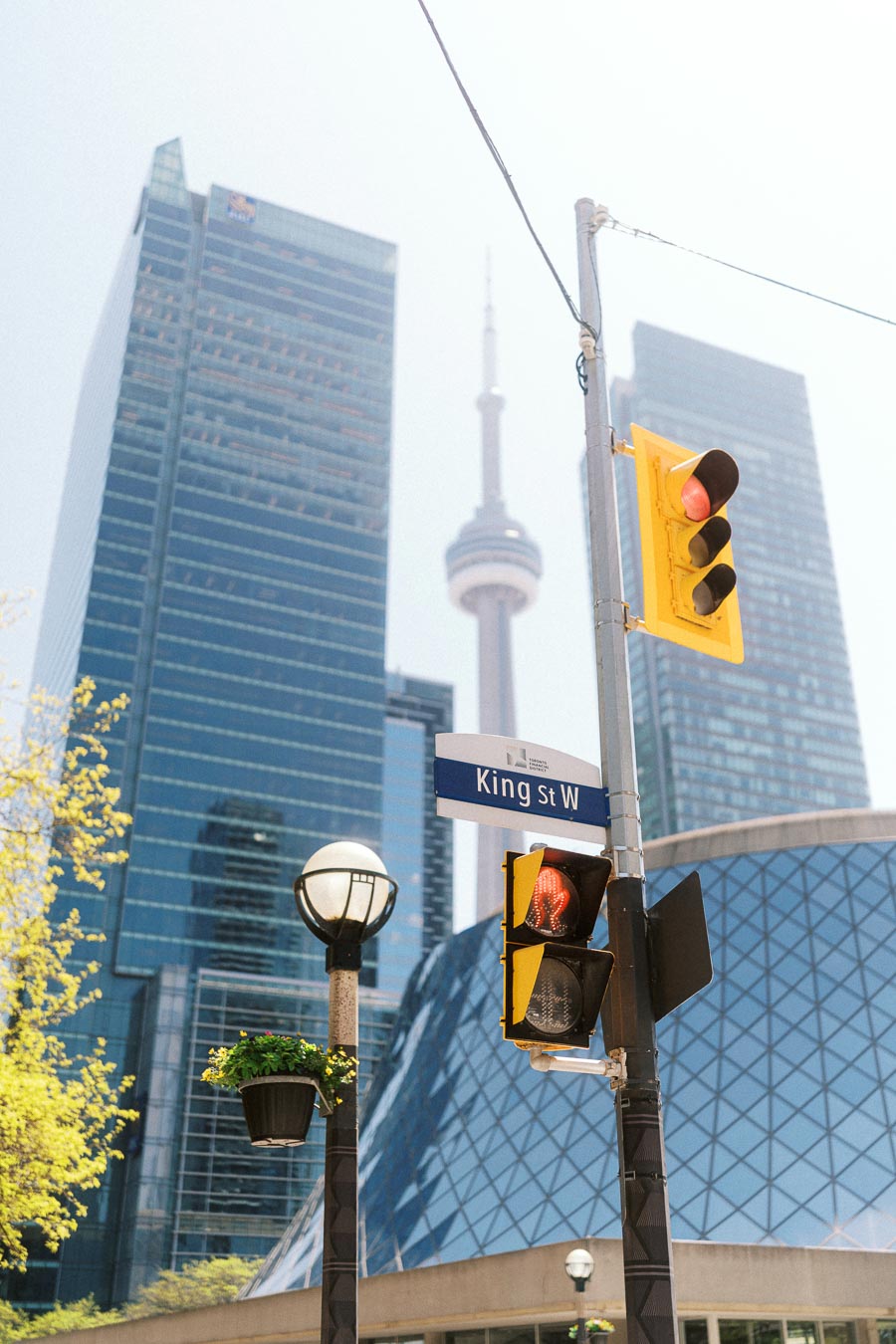 King Street West street sign, red traffic light, and CN Tower with modern skyscrapers in downtown Toronto on a sunny day.