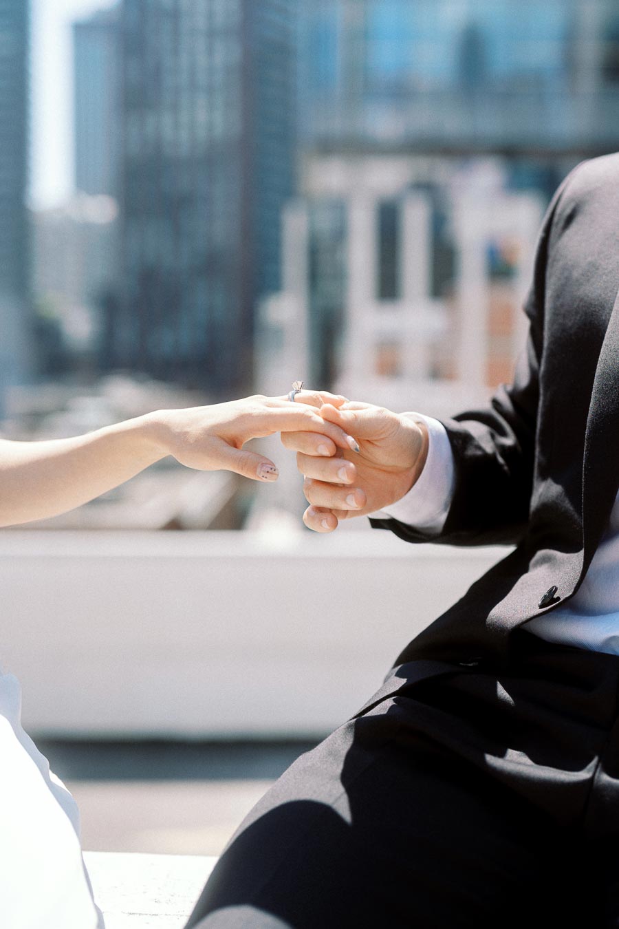 Close-up of couple's hands, one wearing an engagement ring, with downtown Toronto buildings softly blurred in the background.