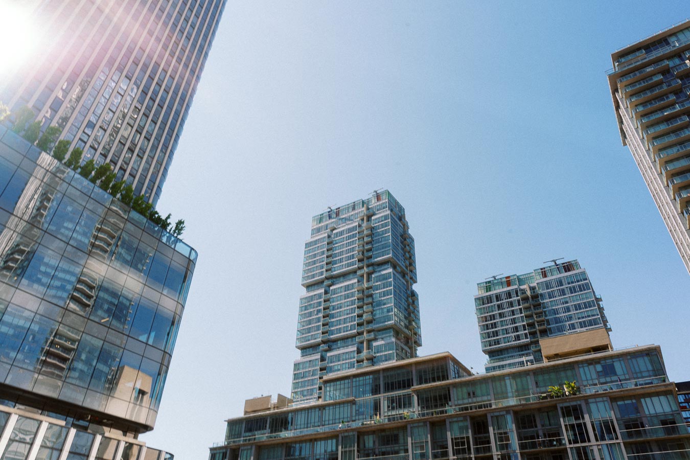 Contemporary high-rise glass buildings in downtown Toronto with sunlight and blue sky above.