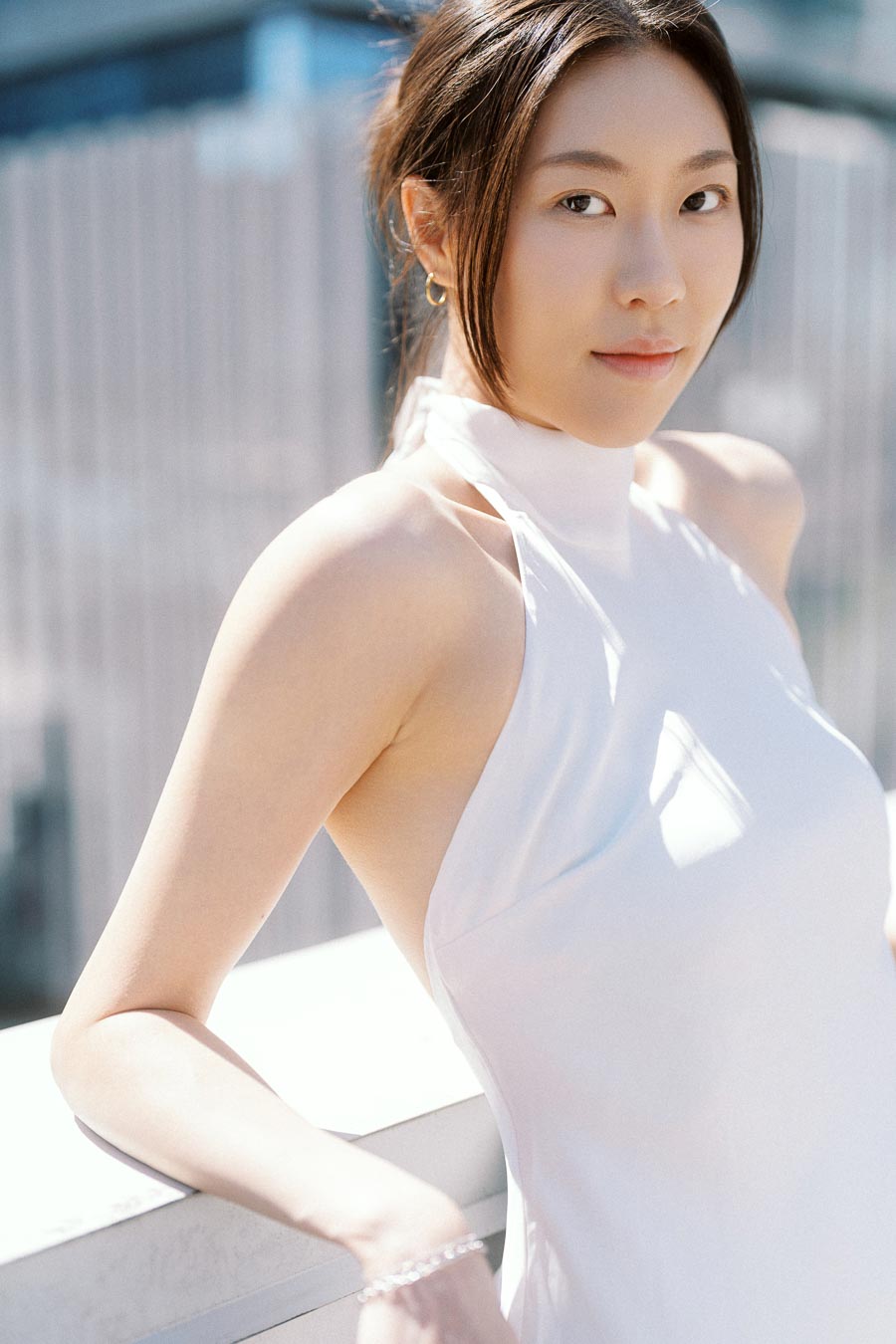 Woman in a white dress posing on a rooftop in downtown Toronto with soft sunlight and city buildings behind her.