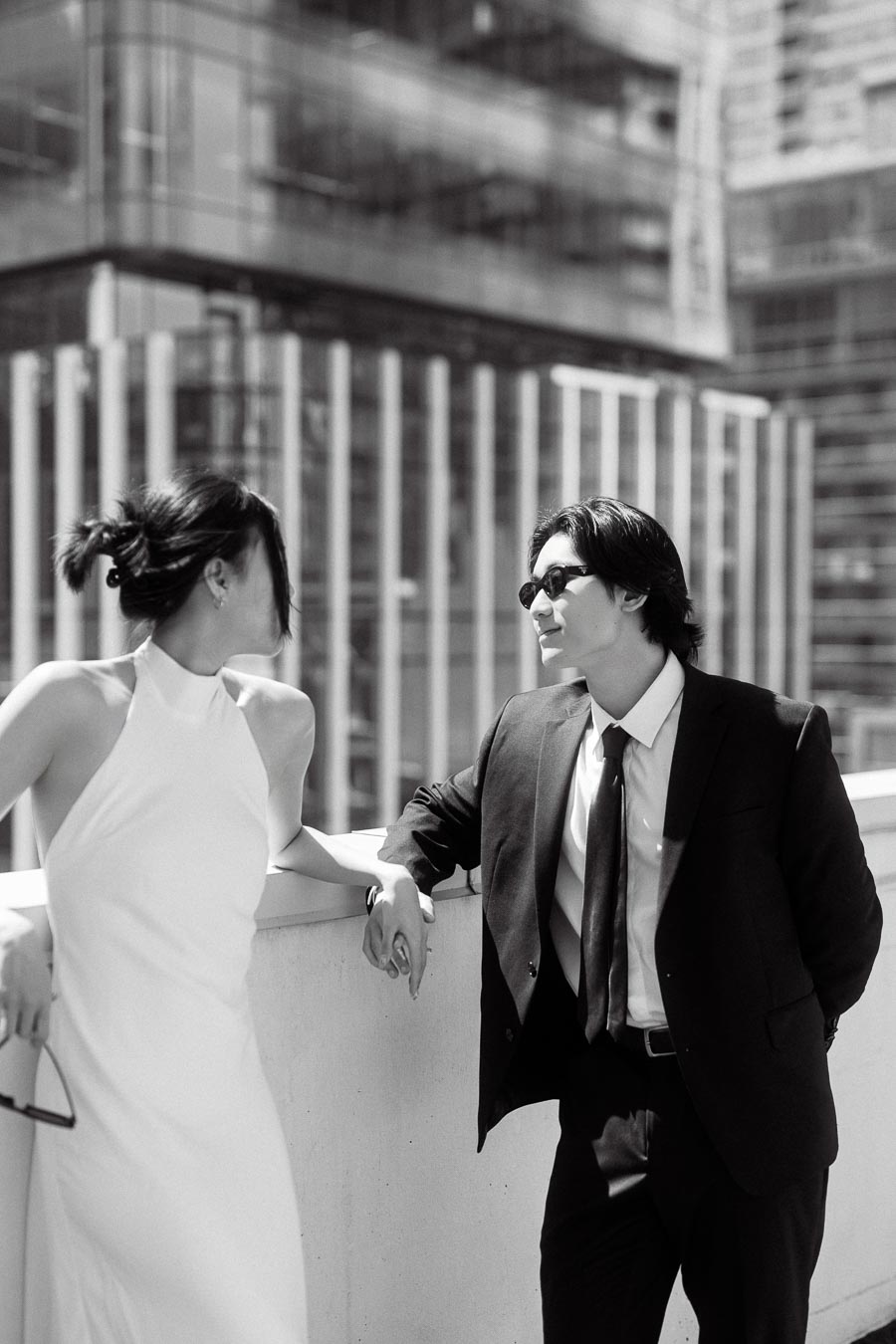 Couple in formal attire holding hands and smiling on a rooftop with downtown Toronto skyscrapers in the background.