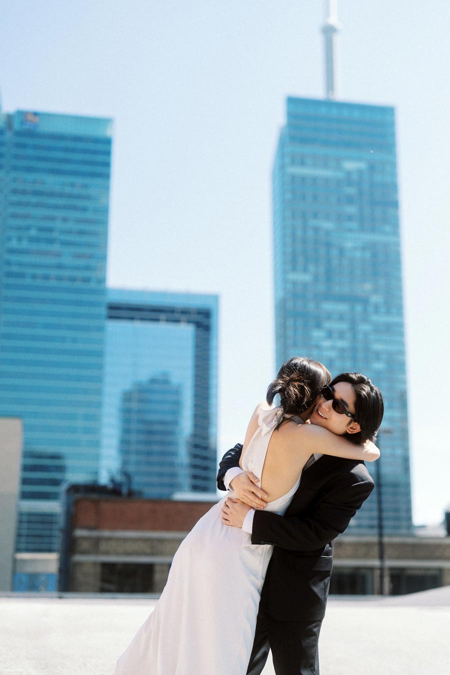Couple embracing on a rooftop with Toronto skyscrapers and CN Tower in the background during an engagement photoshoot.