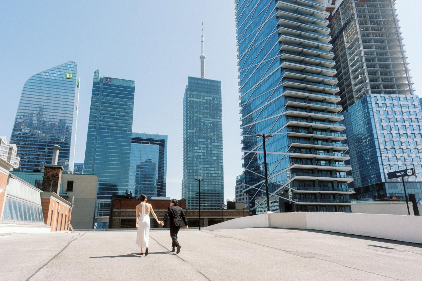 Two people holding hands and walking on a rooftop parking lot with Toronto skyscrapers in the background.