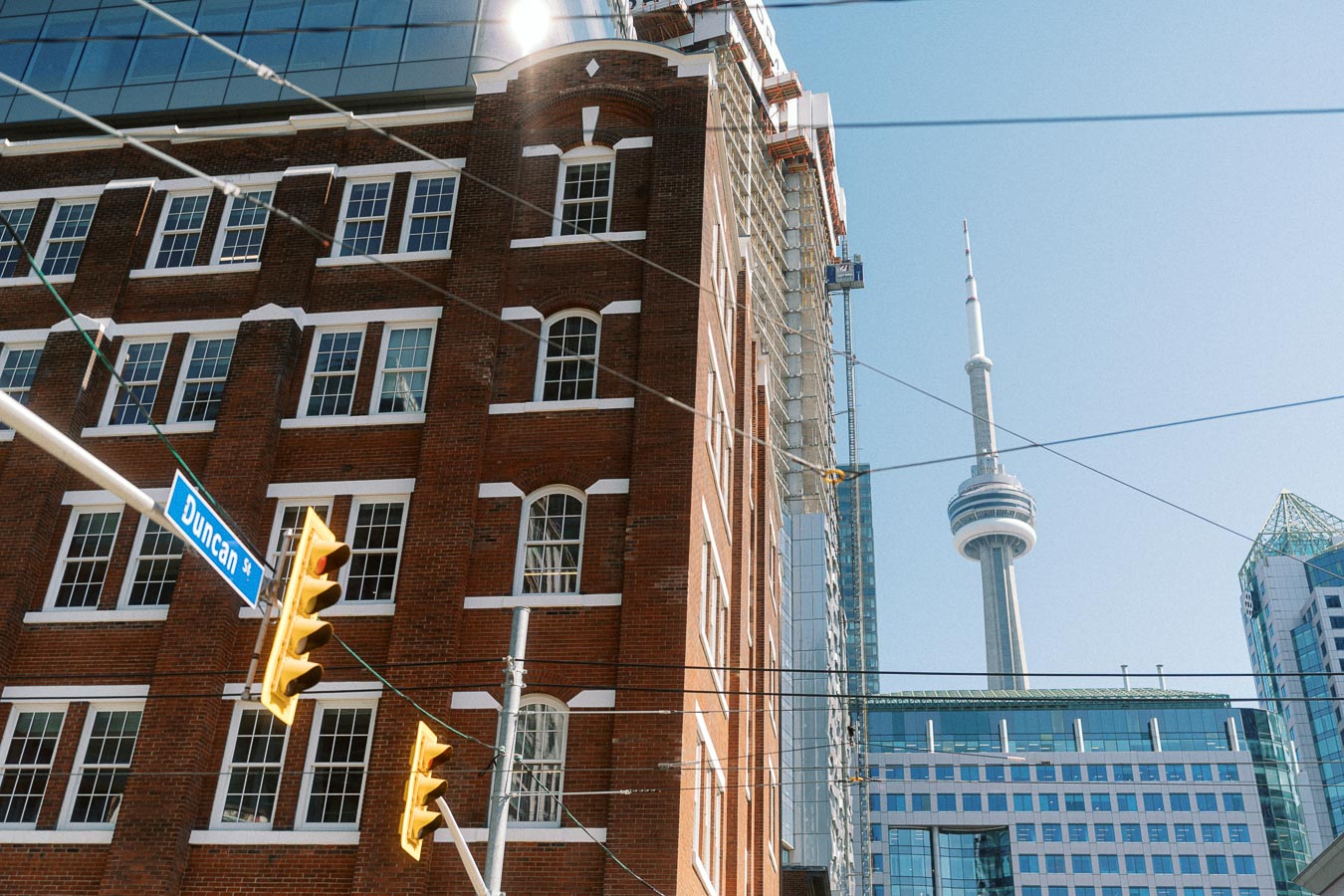 Downtown Toronto street corner with Duncan Street sign, red brick building, traffic lights, and CN Tower in the background on a clear day.