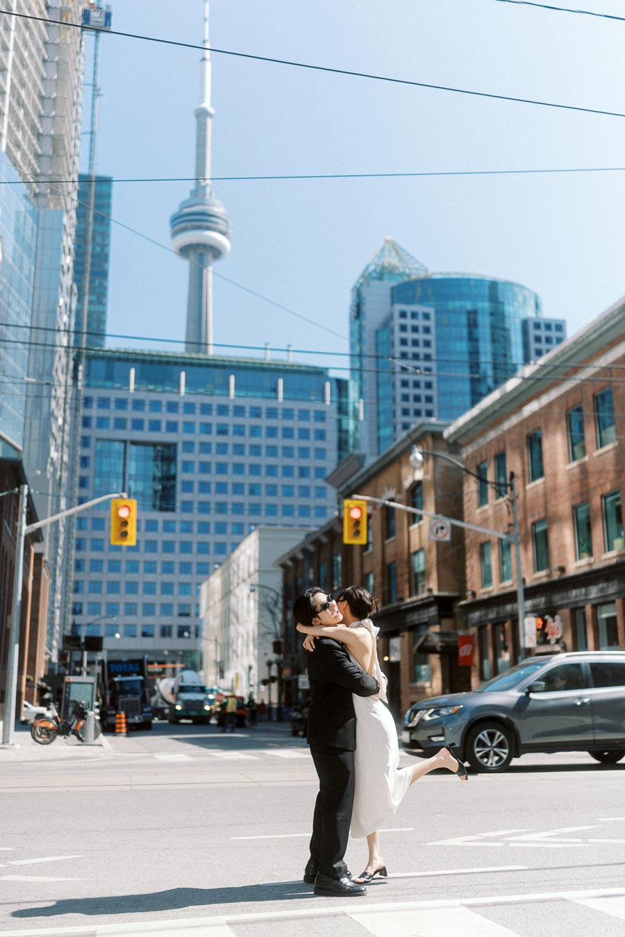 Couple embracing in a crosswalk with the CN Tower and modern downtown Toronto buildings in the background.