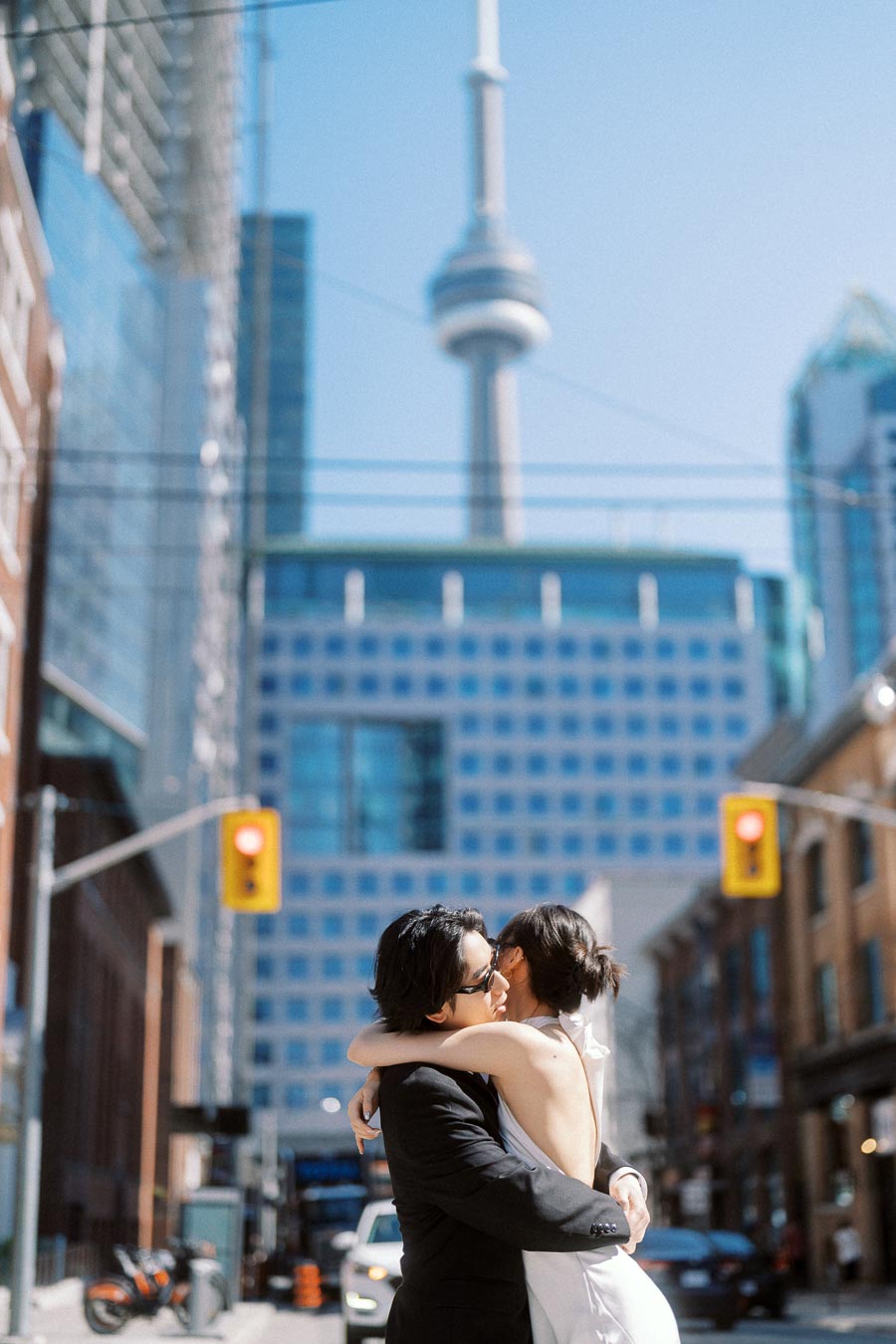 Couple embracing on a downtown Toronto street with the CN Tower and city buildings in the background.