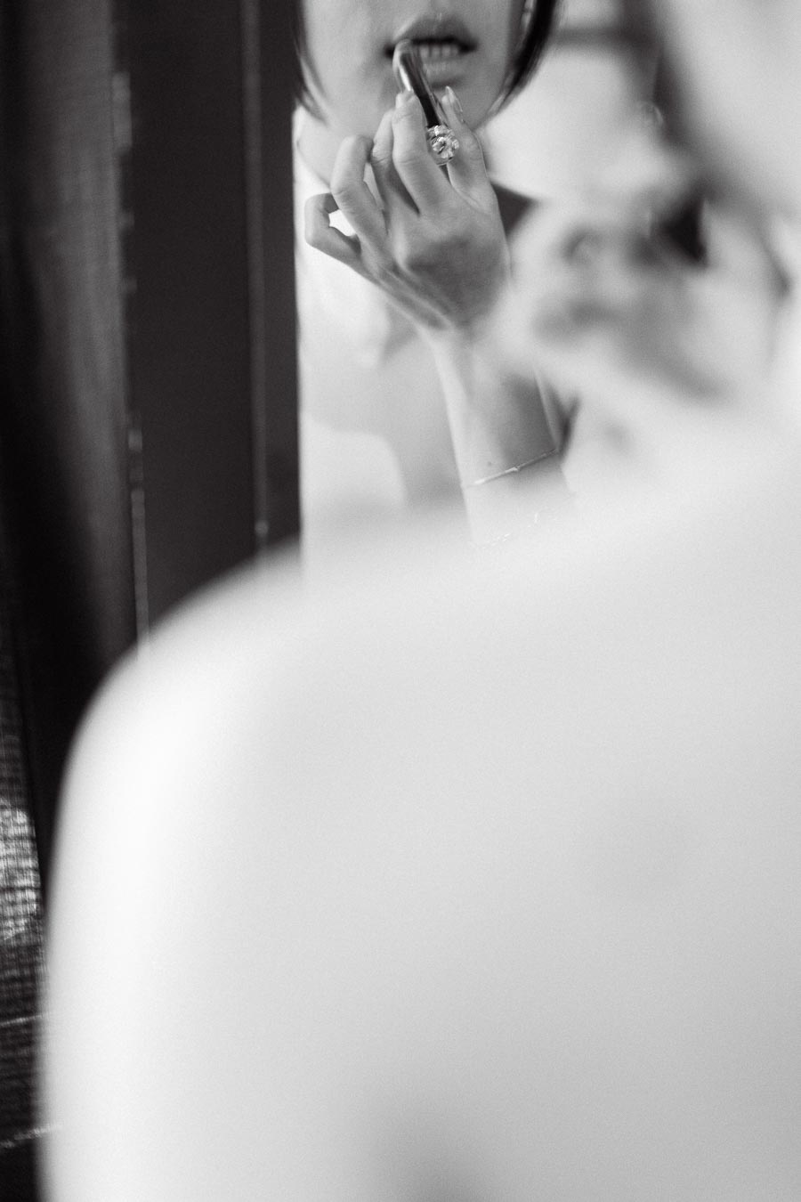 Close-up reflection of a person applying lipstick in a mirror, with soft focus and delicate lighting.