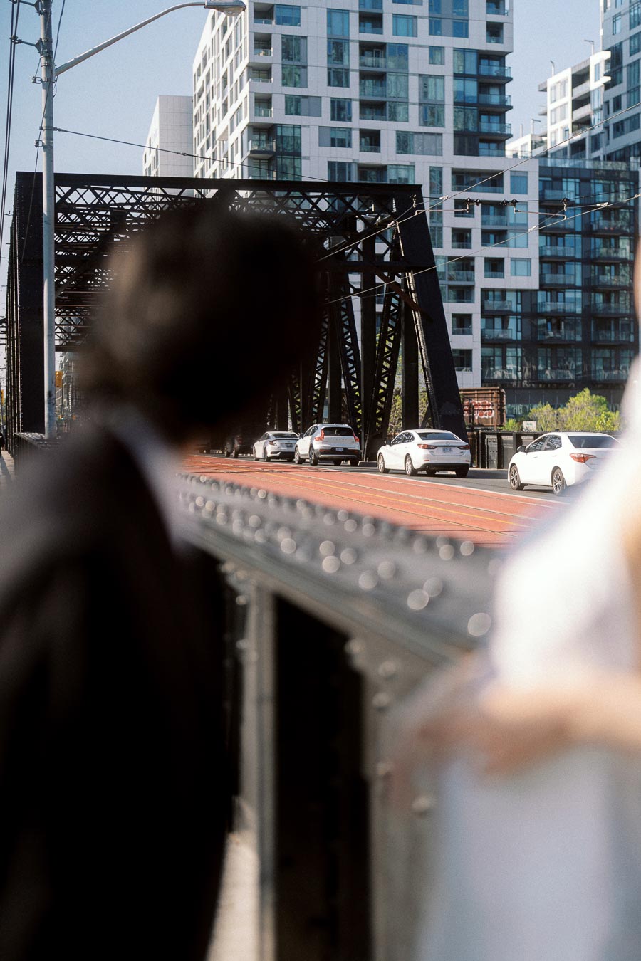 Blurred couple in foreground with Sir Isaac Brock Bridge and modern high-rise buildings in downtown Toronto.