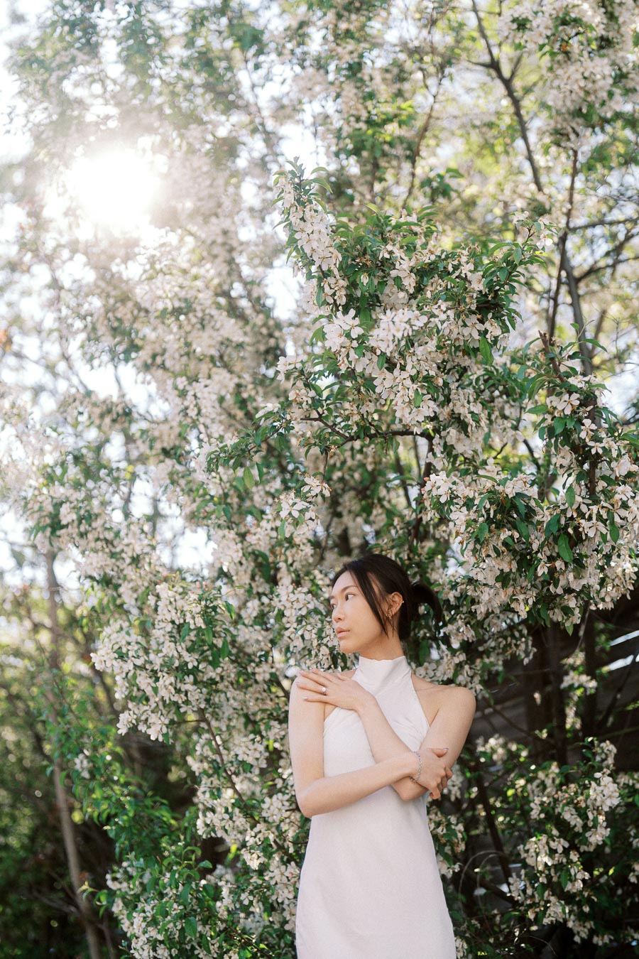 Woman in a white dress standing among blooming branches with sunlight filtering through the trees in Ontario.