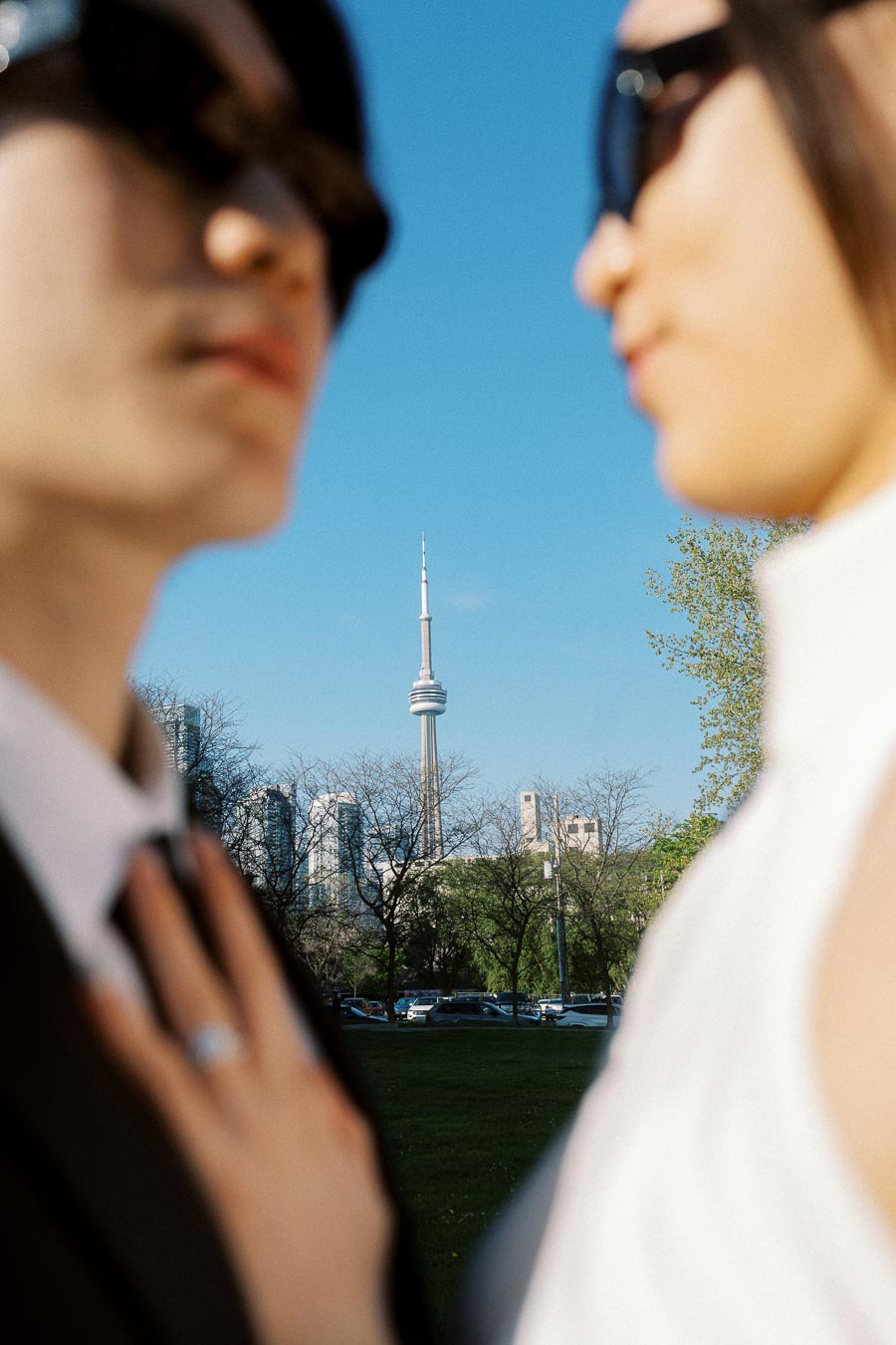 Couple in sunglasses out of focus, with CN Tower and Toronto skyline sharply visible between them on a sunny day.