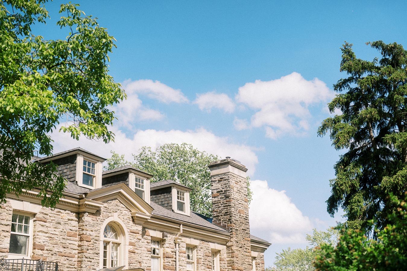 Stone exterior and chimney of Paletta Mansion with leafy trees and blue sky.