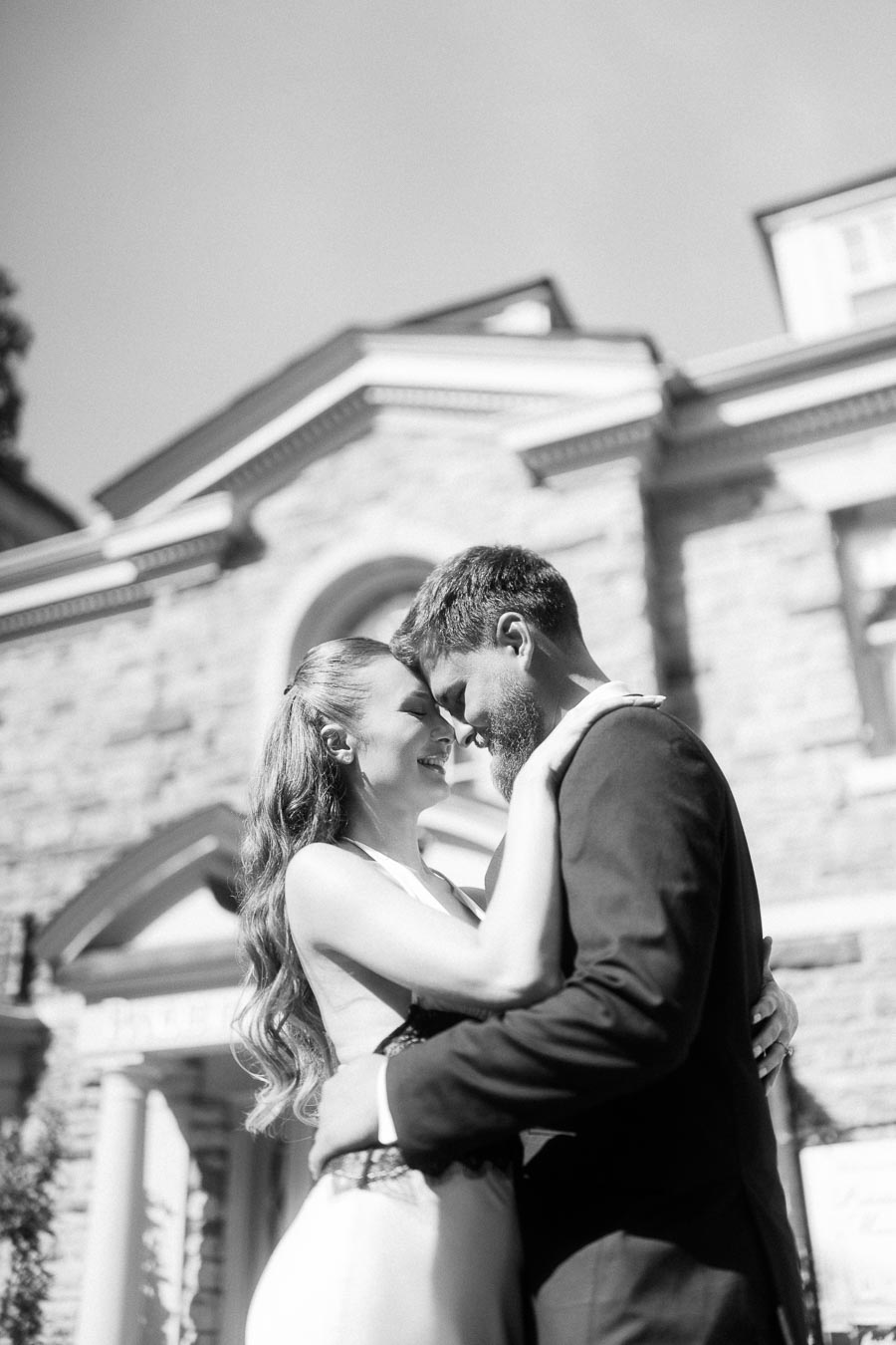 Anastasiia and Petr embrace in front of Paletta Mansion's stone entrance, captured in black and white.