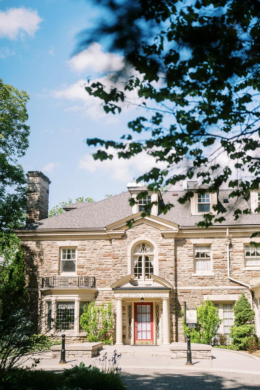Paletta Mansion stone facade and entrance surrounded by greenery on a sunny afternoon.