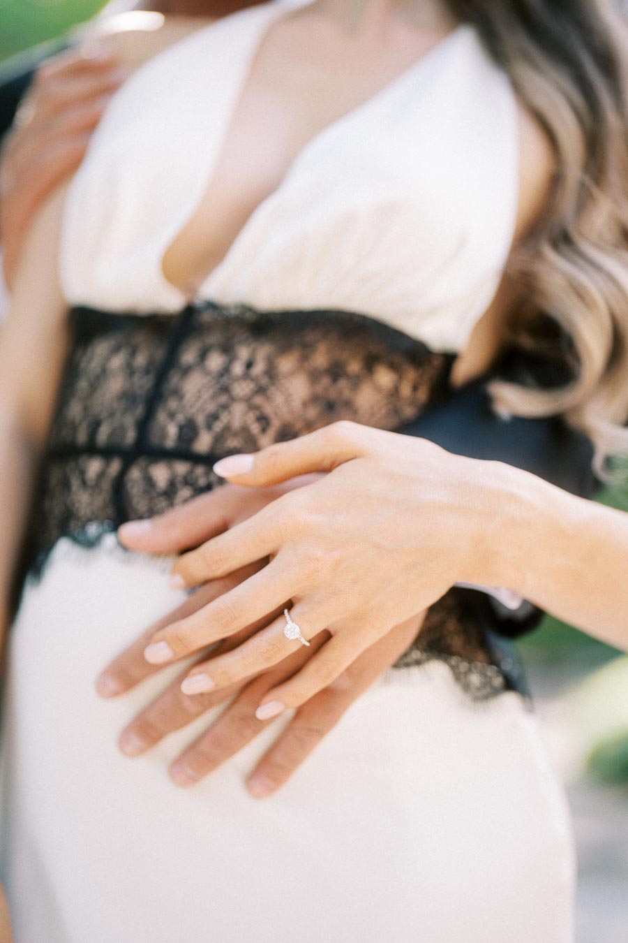 Anastasiia's hand with engagement ring resting over Petr's hand against white and black lace dress.