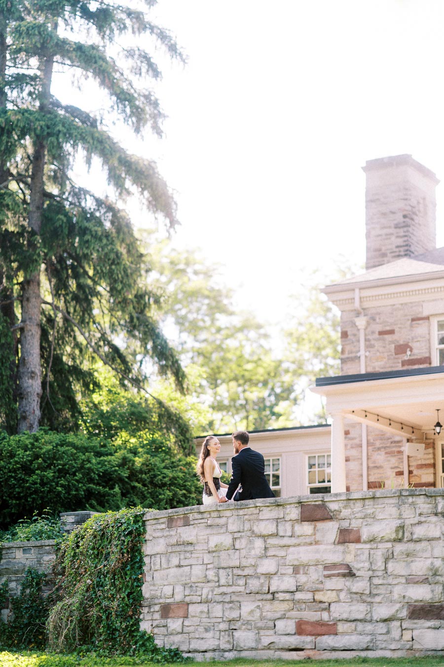 Anastasiia and Petr holding hands on a stone terrace with greenery and mansion in background.