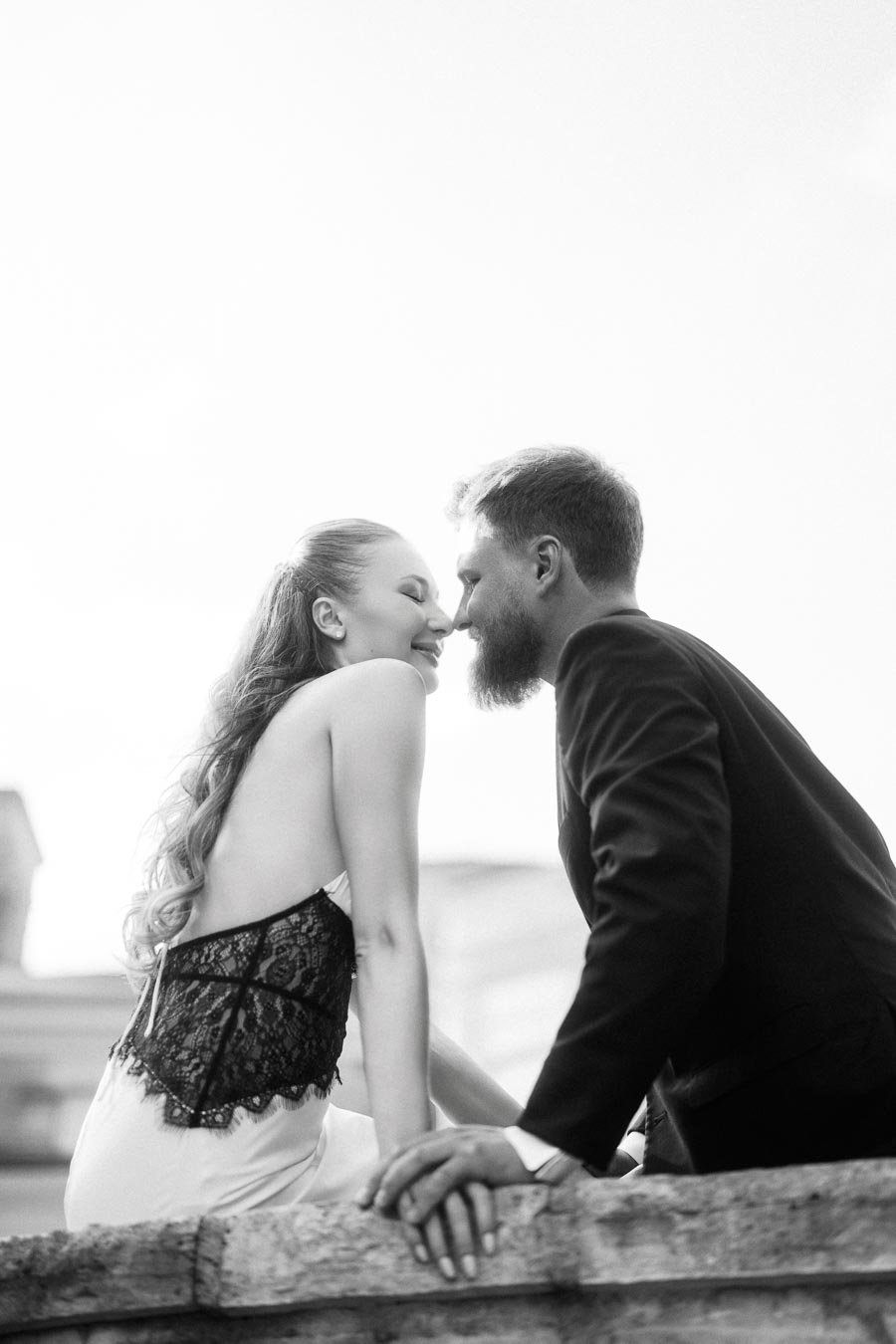 Anastasiia and Petr leaning close together on a stone railing, black and white photo.