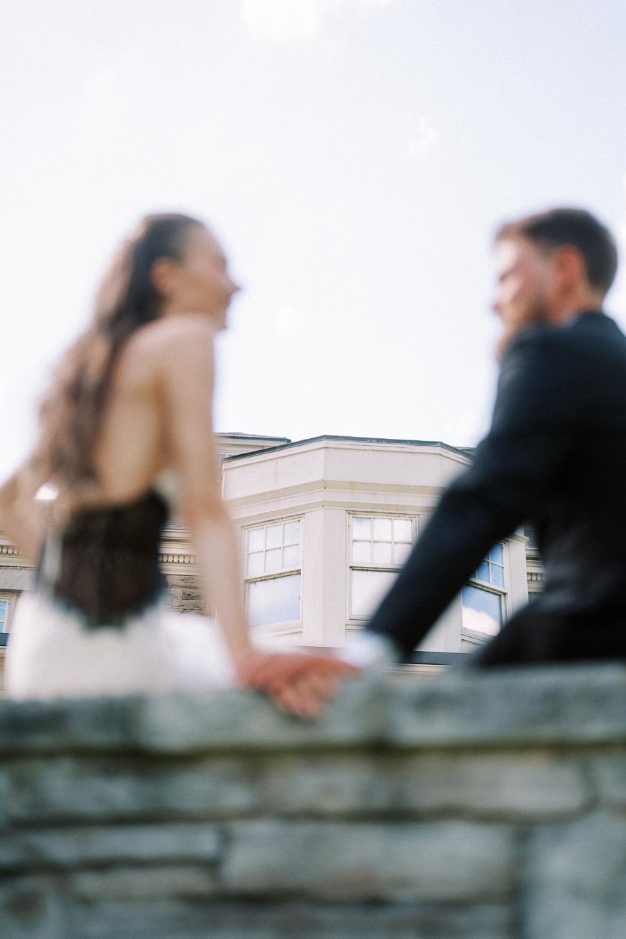 Blurred engaged couple holding hands in front of Paletta Mansion's upper windows and stone wall.