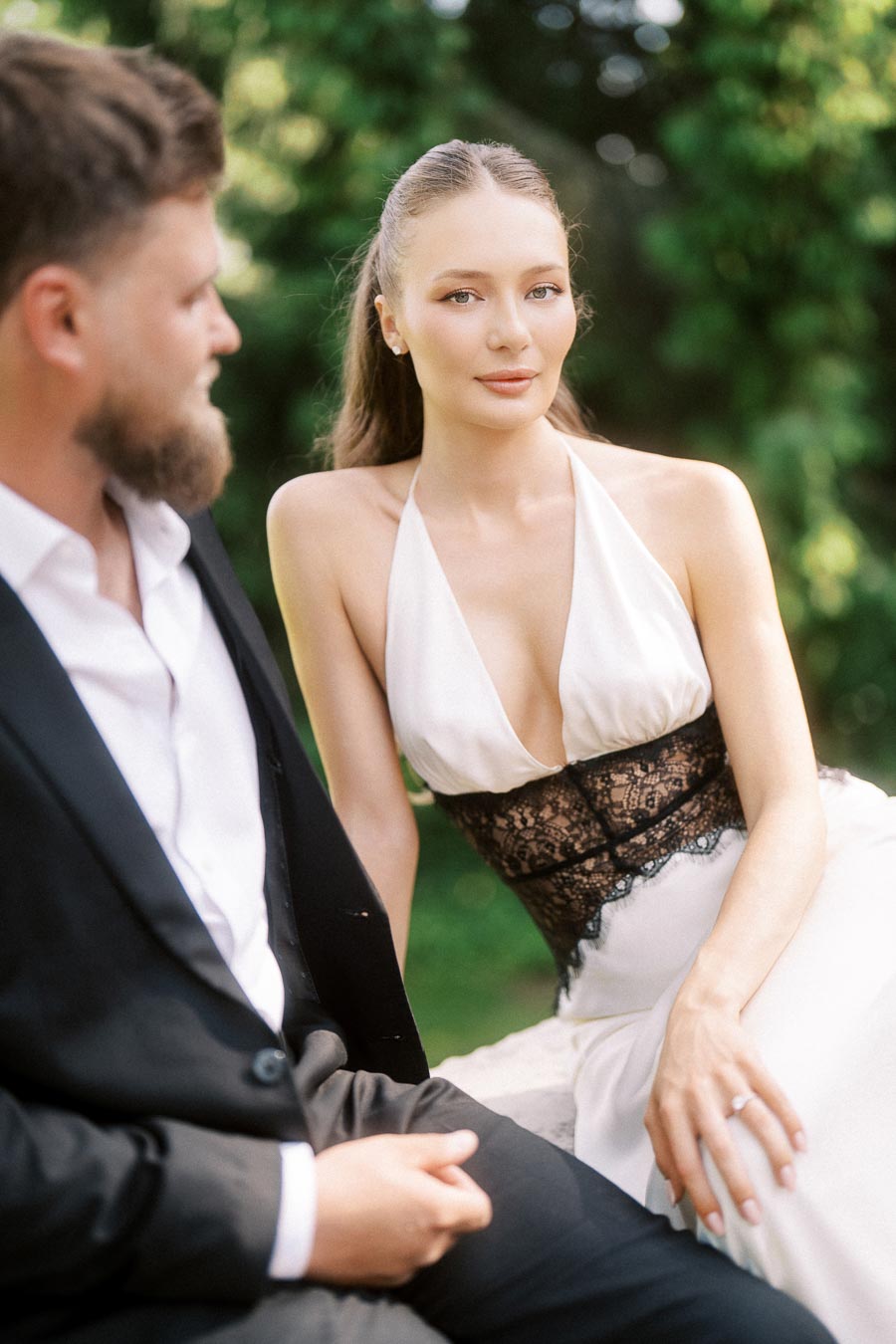 Anastasiia and Petr sitting together outdoors, Anastasiia facing camera, green trees behind.