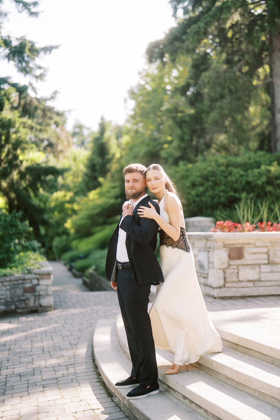 Engaged couple posing on curved stone steps with garden and stone wall in background.