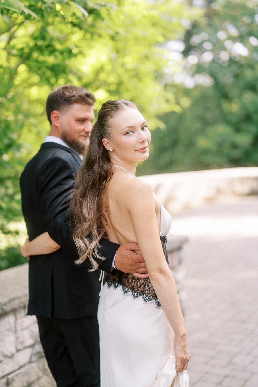 Anastasiia and Petr pose together on a stone pathway surrounded by green foliage.