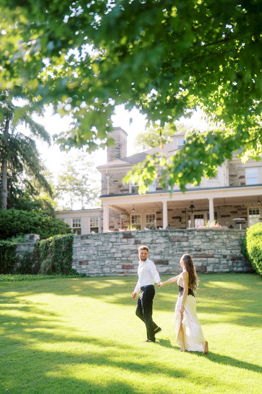 Anastasiia and Petr walk hand in hand on a bright green lawn with Paletta Mansion in the background.