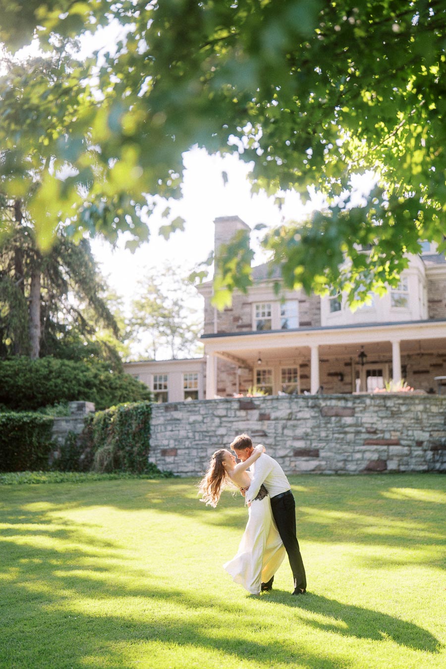 Anastasiia and Petr dancing together on a sunlit lawn in front of Paletta Mansion, framed by green trees.