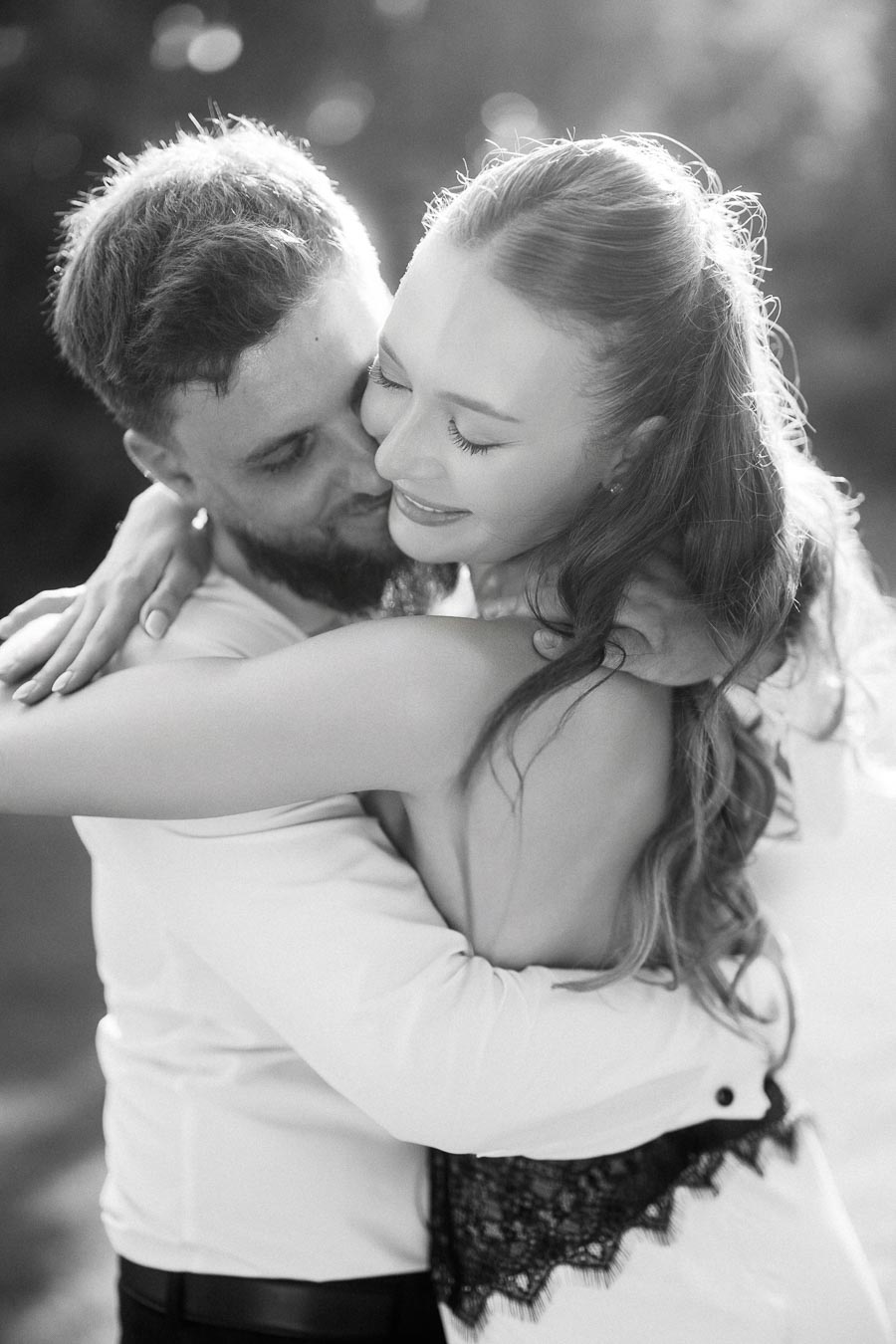 Anastasiia and Petr hugging closely in black and white, sunlight highlighting their faces and hair.