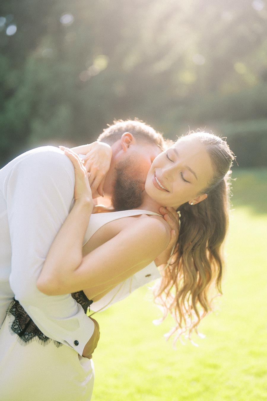 Anastasiia and Petr in a close embrace on a sunlit lawn, surrounded by greenery.