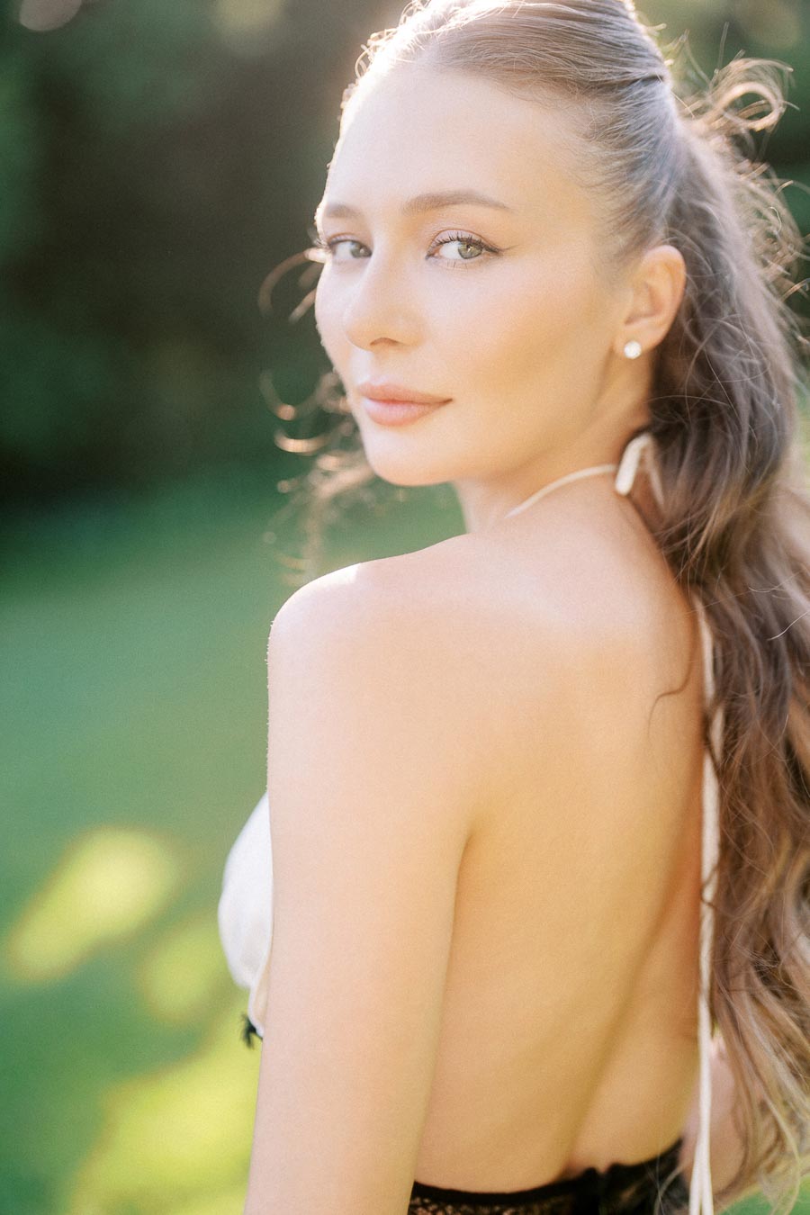 Close-up portrait of Anastasiia outdoors, looking over her shoulder with sunlight on her face.