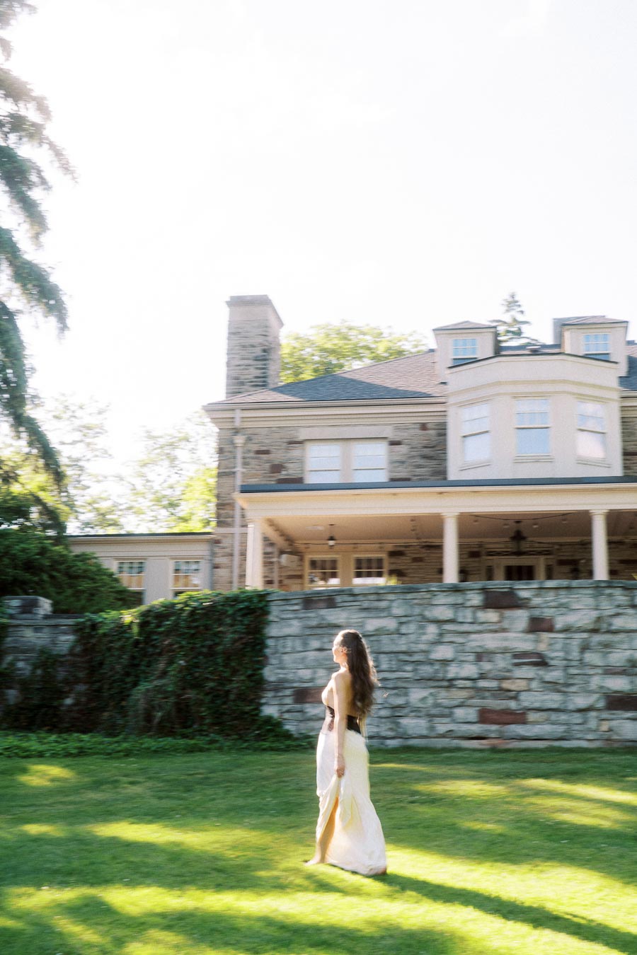 Anastasiia in a flowing dress walking on the lawn in front of Paletta Mansion's stone facade.