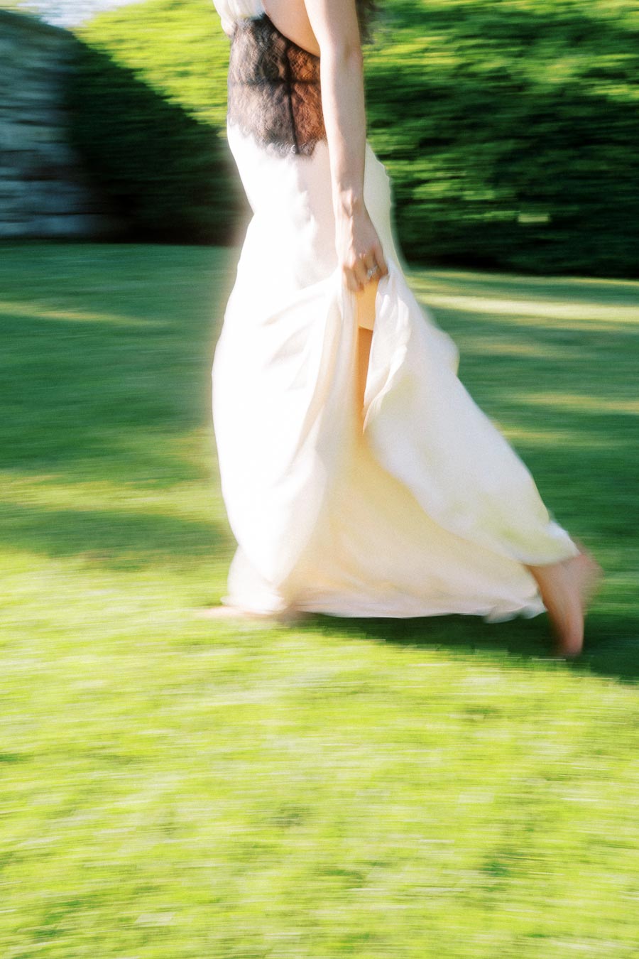 Woman in a white dress walking barefoot with motion blur on green lawn outdoors.