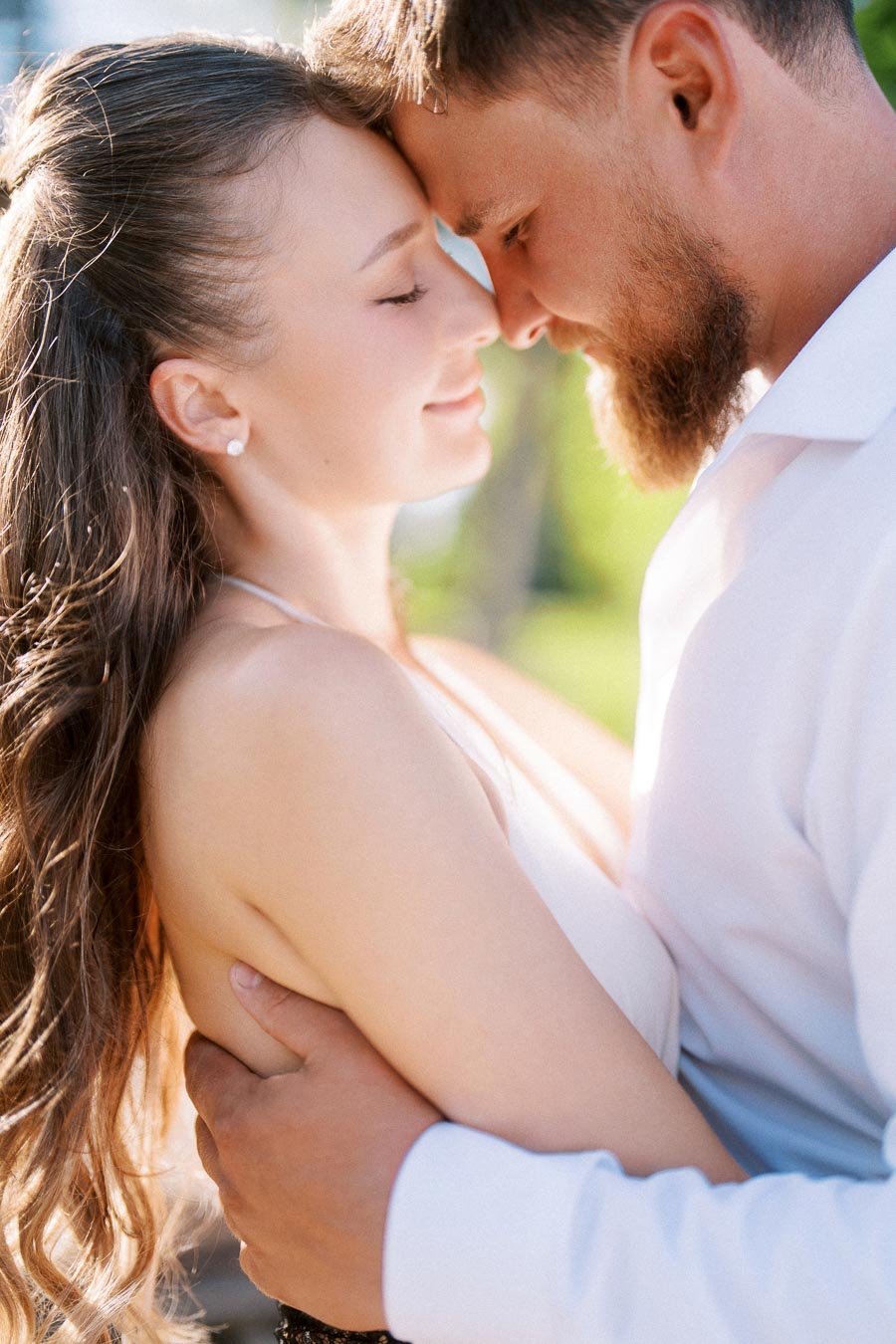 Engaged couple standing close together with foreheads touching in natural light.