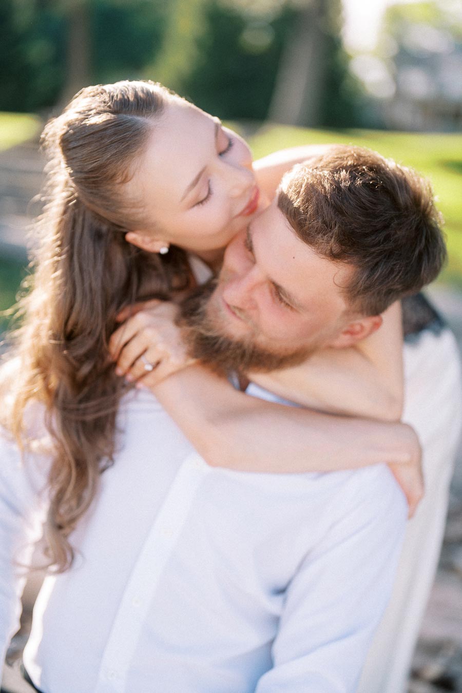 Anastasiia giving Petr a piggyback hug with sunlight on their faces outdoors.