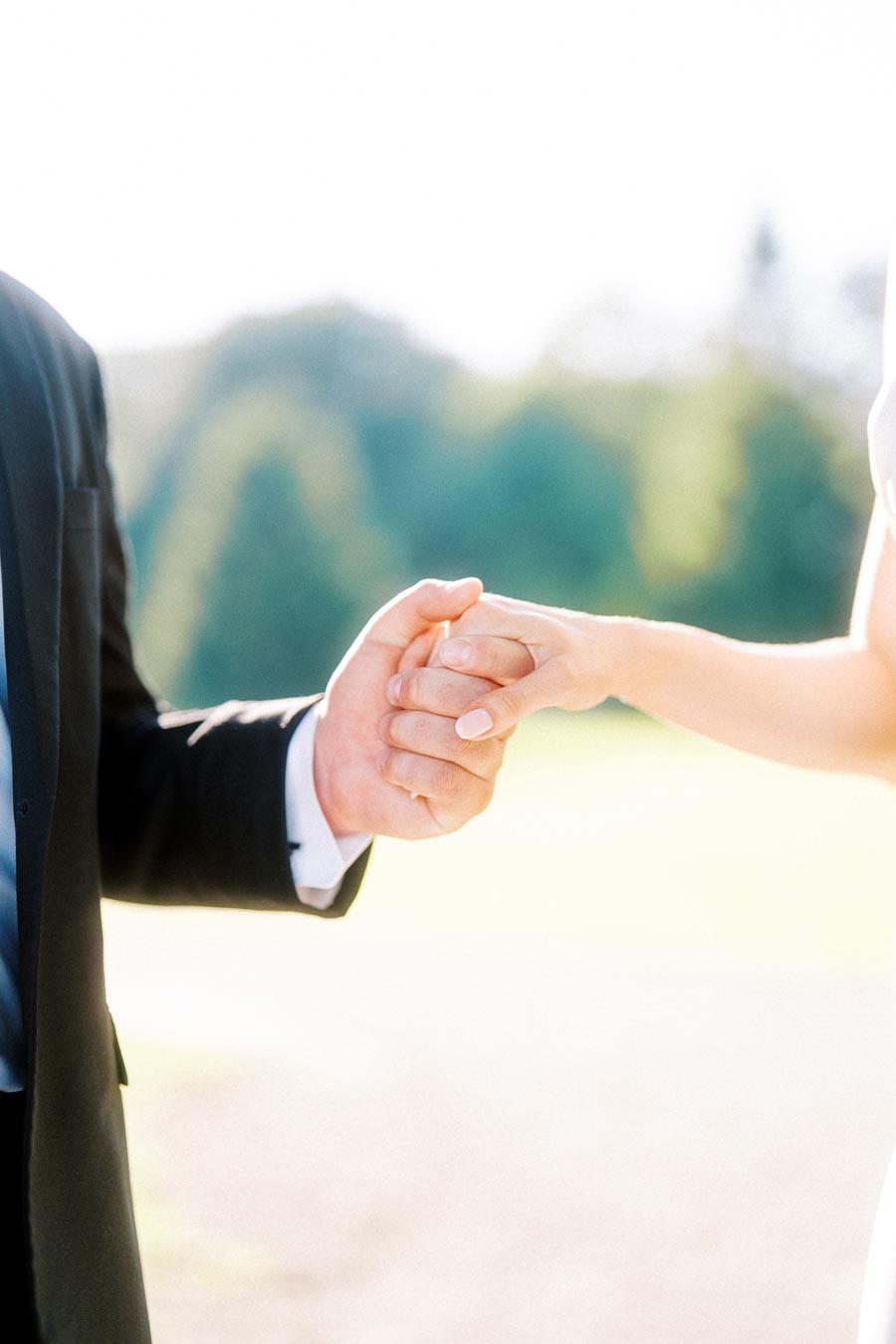 Close-up of two people holding hands, one in a suit, outdoors with soft background.