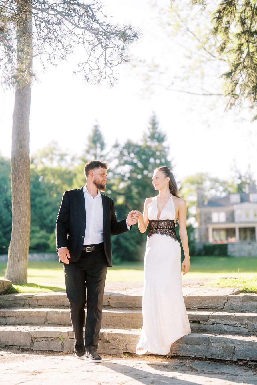 Anastasiia and Petr walking together down stone steps in sunlight, trees and house in background.