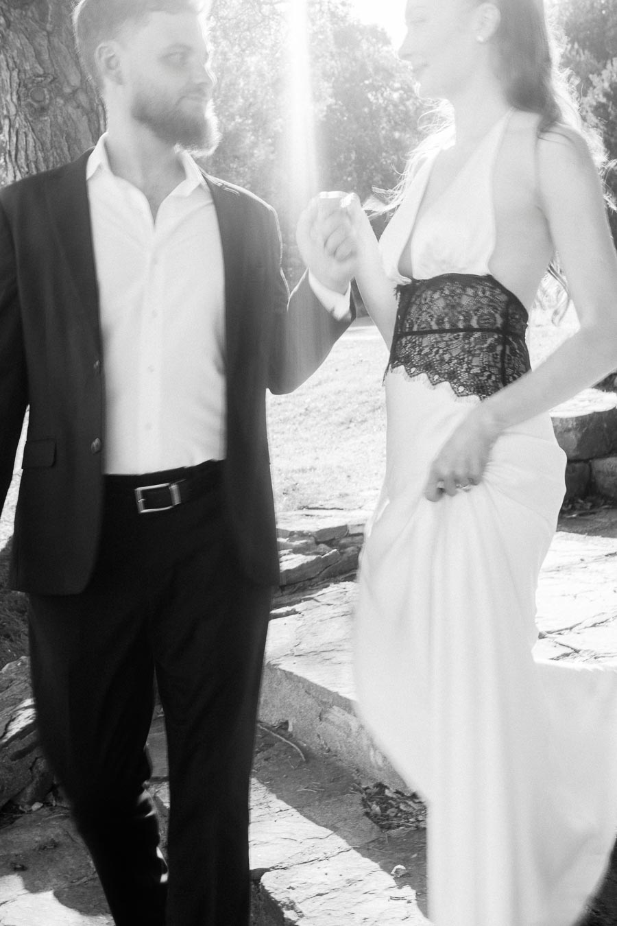 Anastasiia and Petr holding hands while walking on a stone path in bright sunlight, black and white photo.