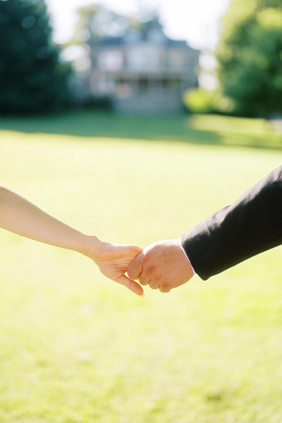 Two people holding hands on a bright green lawn with a blurred mansion in the distance.